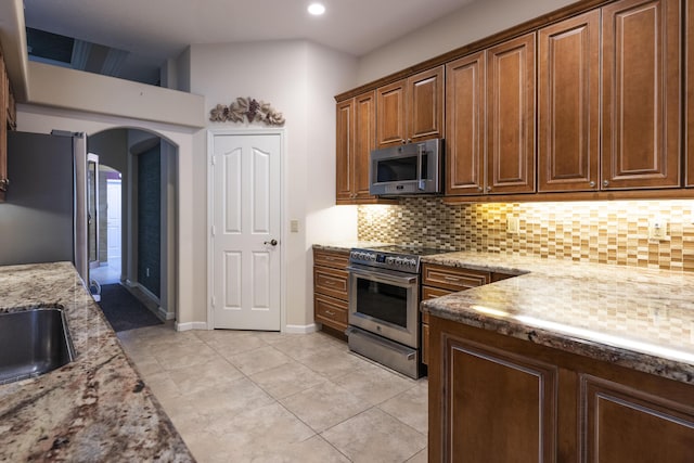 kitchen with light tile patterned floors, stainless steel appliances, backsplash, and light stone countertops