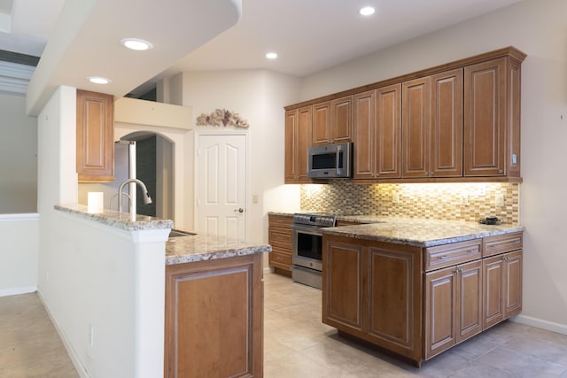 kitchen featuring light stone counters, kitchen peninsula, stainless steel appliances, and tasteful backsplash