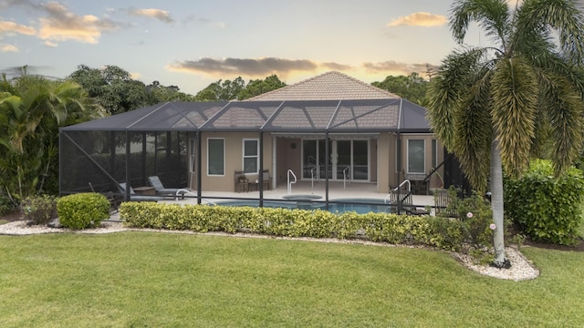 back house at dusk featuring a swimming pool with hot tub, a lanai, a yard, and a patio