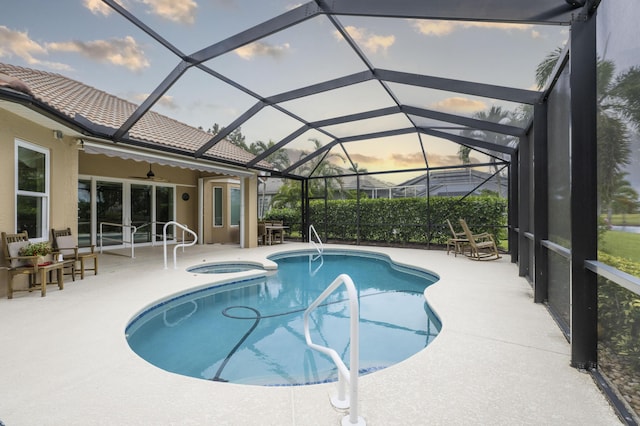 pool at dusk featuring ceiling fan, a patio, glass enclosure, and an in ground hot tub