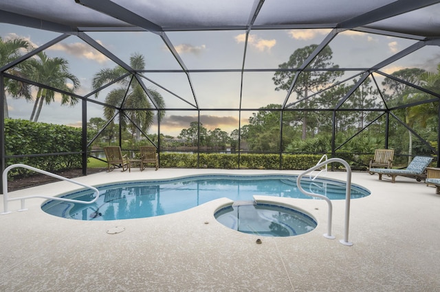 pool at dusk with an in ground hot tub, a lanai, and a patio area