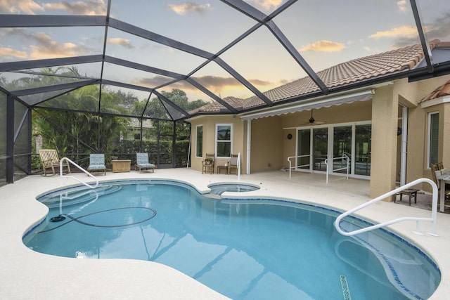 pool at dusk featuring ceiling fan, glass enclosure, an in ground hot tub, and a patio