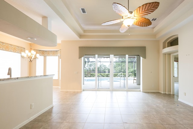 tiled spare room with ceiling fan with notable chandelier and a tray ceiling