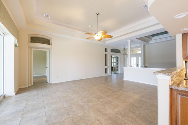 unfurnished living room with a raised ceiling, light tile patterned floors, ceiling fan with notable chandelier, and ornamental molding