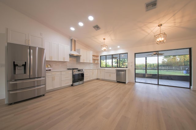 kitchen with wall chimney exhaust hood, ceiling fan with notable chandelier, stainless steel appliances, decorative light fixtures, and white cabinetry