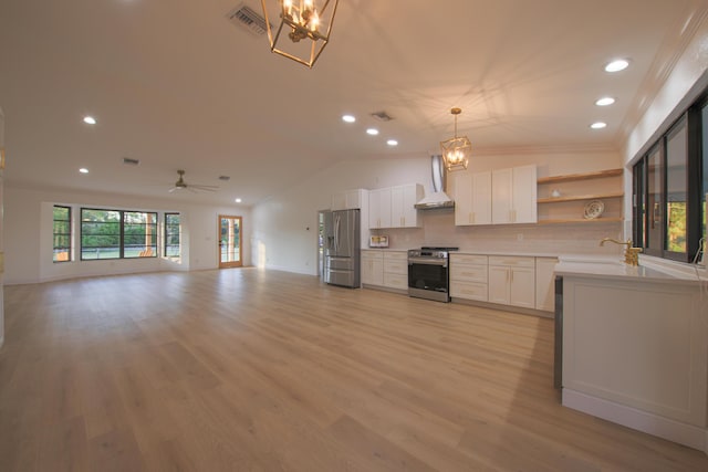 kitchen featuring lofted ceiling, white cabinets, wall chimney range hood, appliances with stainless steel finishes, and decorative light fixtures