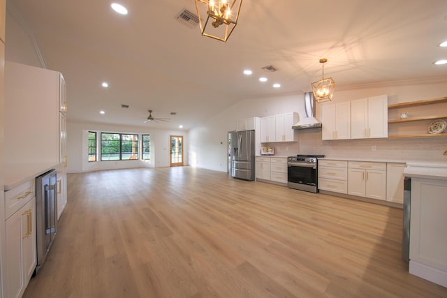 kitchen featuring ceiling fan with notable chandelier, wall chimney range hood, decorative light fixtures, white cabinetry, and stainless steel appliances