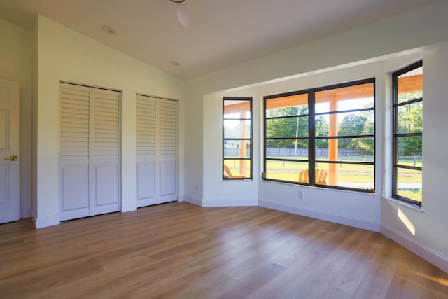 unfurnished bedroom with lofted ceiling, light hardwood / wood-style floors, and two closets