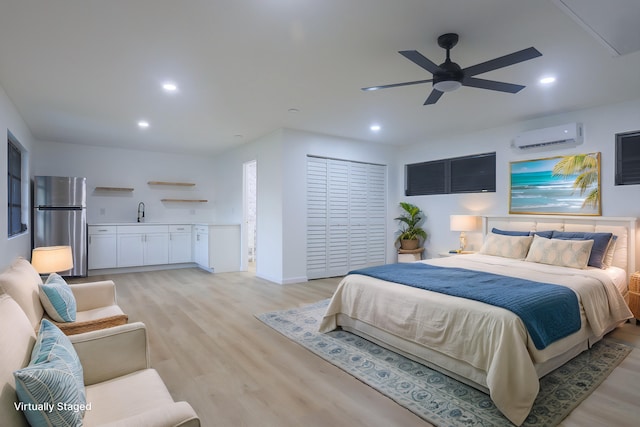 bedroom with a wall mounted air conditioner, sink, light hardwood / wood-style flooring, ceiling fan, and stainless steel fridge