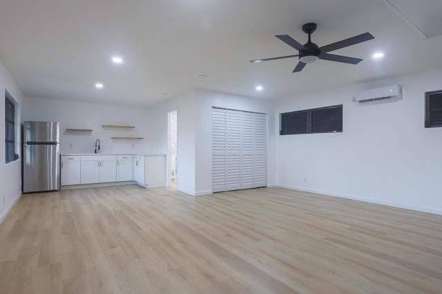 unfurnished living room with a wall mounted AC, ceiling fan, sink, and light wood-type flooring