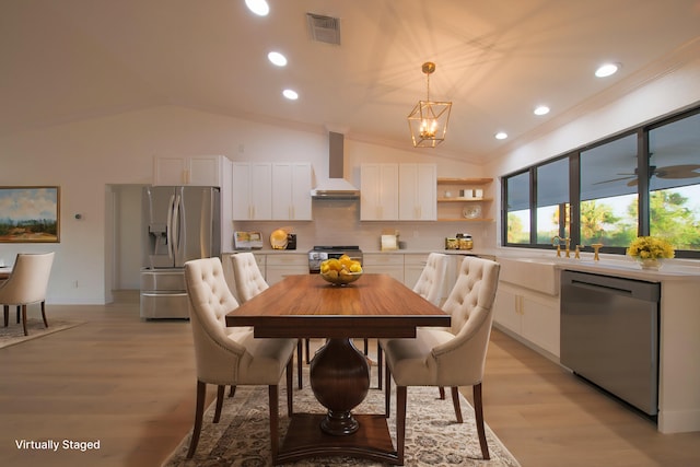 dining room with light wood-type flooring, ceiling fan with notable chandelier, vaulted ceiling, crown molding, and sink