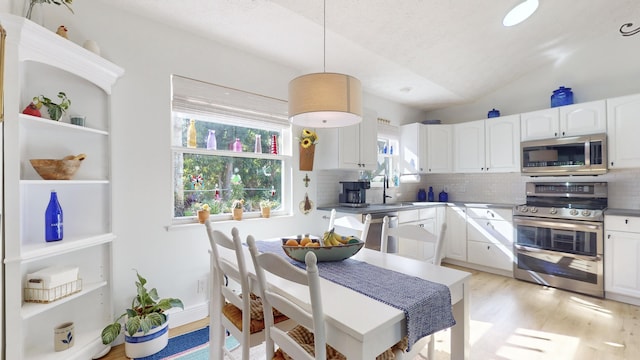 kitchen featuring white cabinets, decorative light fixtures, lofted ceiling, and stainless steel appliances