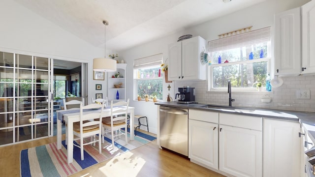 kitchen with lofted ceiling, white cabinets, sink, stainless steel dishwasher, and decorative light fixtures