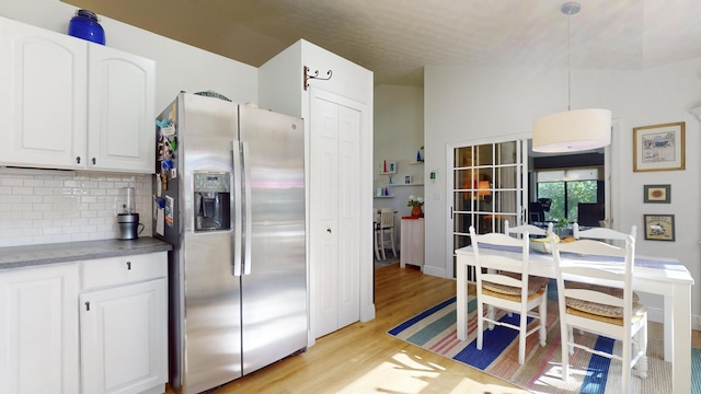 kitchen with white cabinets, light hardwood / wood-style flooring, decorative backsplash, stainless steel fridge, and decorative light fixtures