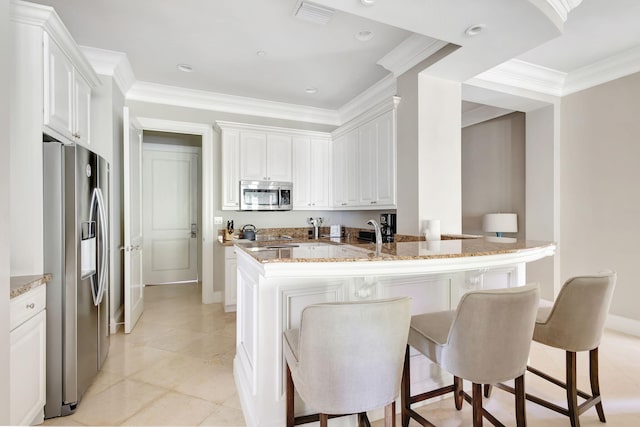 kitchen with white cabinets, appliances with stainless steel finishes, a kitchen bar, and light stone counters