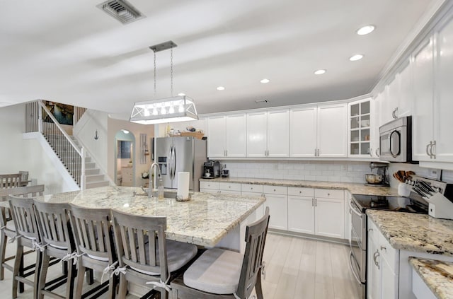 kitchen with a kitchen island with sink, white cabinetry, pendant lighting, and appliances with stainless steel finishes