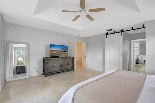 bedroom featuring a barn door, a tray ceiling, ensuite bath, and ceiling fan