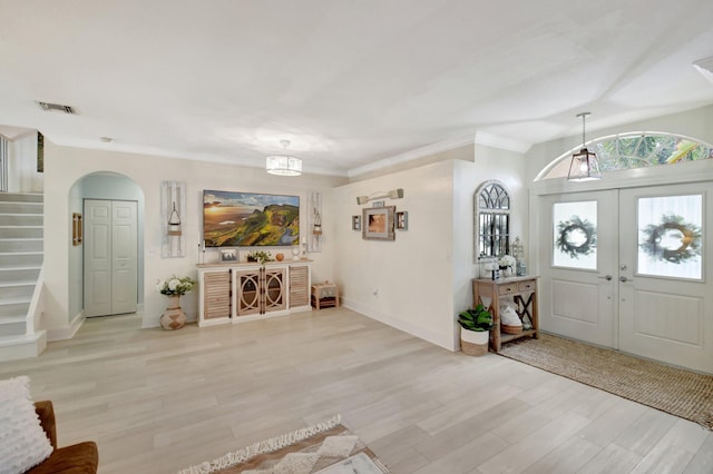 entryway with crown molding, french doors, light hardwood / wood-style floors, and an inviting chandelier