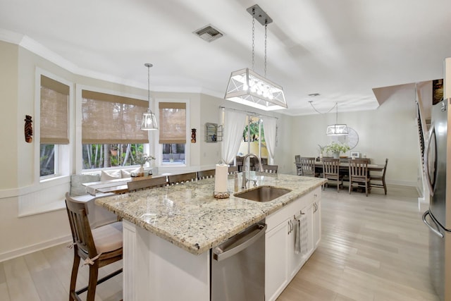 kitchen featuring stainless steel appliances, sink, white cabinets, hanging light fixtures, and an island with sink