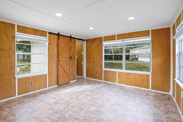 unfurnished room featuring a barn door, wood walls, and a wealth of natural light