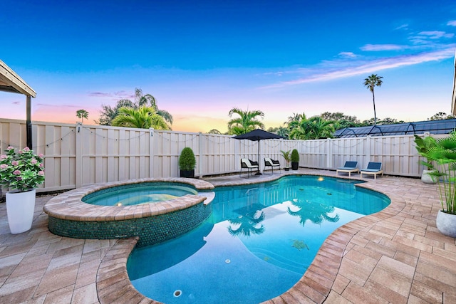 pool at dusk with an in ground hot tub and a patio