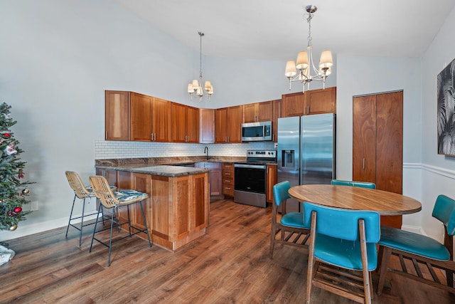 kitchen featuring dark wood-type flooring, appliances with stainless steel finishes, an inviting chandelier, decorative light fixtures, and kitchen peninsula