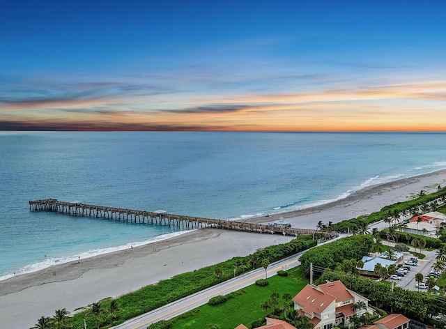 aerial view at dusk featuring a water view and a beach view