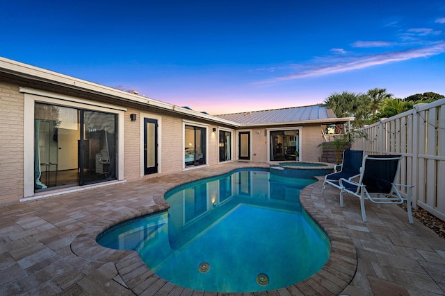 pool at dusk with an in ground hot tub and a patio area