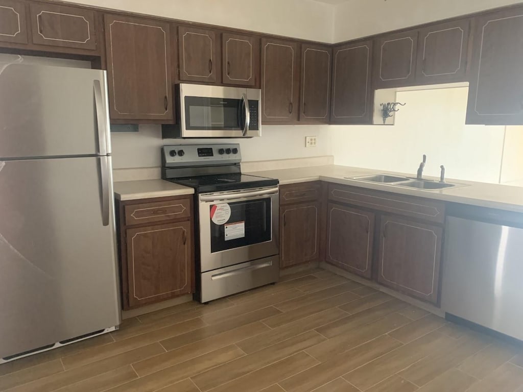 kitchen featuring dark brown cabinetry, sink, light wood-type flooring, and appliances with stainless steel finishes