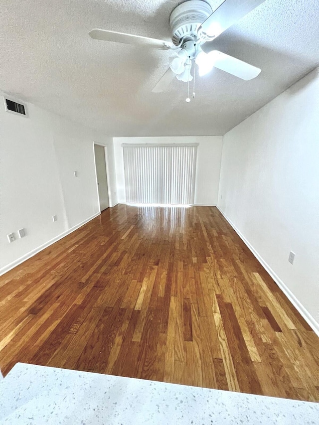 spare room with a ceiling fan, baseboards, wood finished floors, visible vents, and a textured ceiling