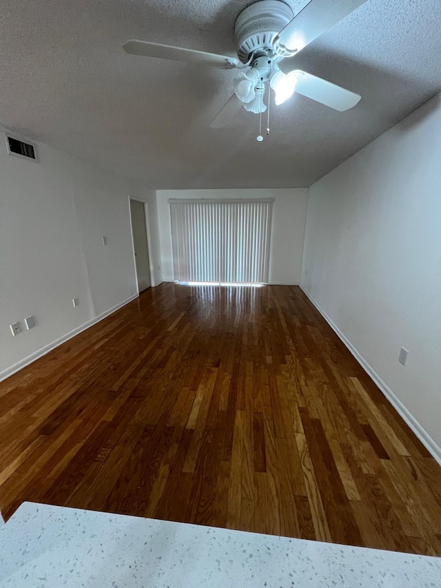 empty room with a ceiling fan, a textured ceiling, visible vents, and wood finished floors