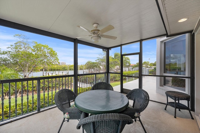 sunroom with ceiling fan and a water view