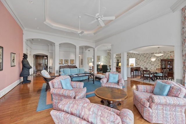 living room with light hardwood / wood-style flooring, ceiling fan, a tray ceiling, ornamental molding, and decorative columns