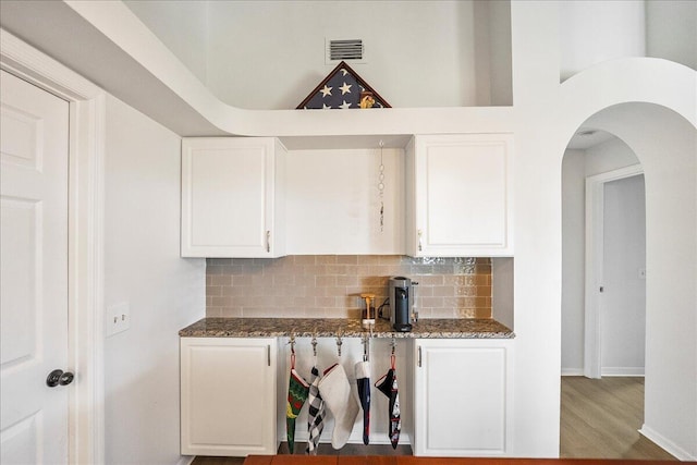 kitchen featuring decorative backsplash, white cabinetry, dark stone counters, and hardwood / wood-style flooring