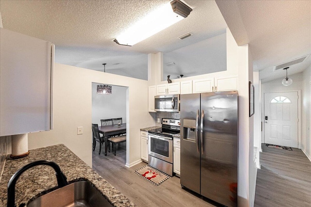 kitchen with stainless steel appliances, sink, dark stone countertops, white cabinetry, and lofted ceiling