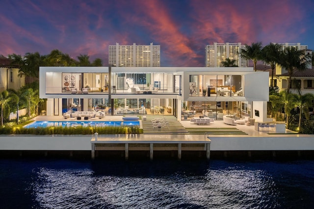 back of property at dusk with an outdoor pool, a water view, a patio, and a balcony