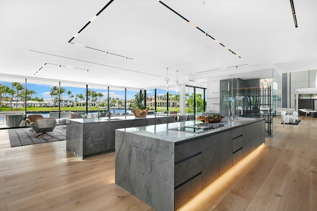 kitchen featuring stainless steel gas stovetop, floor to ceiling windows, a large island with sink, sink, and light wood-type flooring