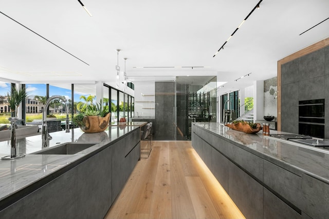 kitchen featuring black double oven, sink, a large island with sink, light hardwood / wood-style flooring, and hanging light fixtures