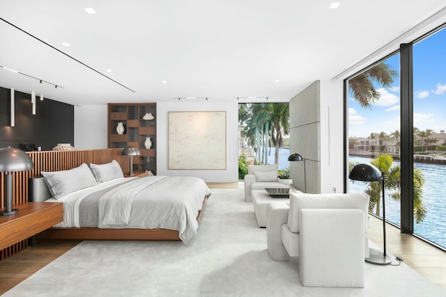 bedroom with a water view, access to exterior, light hardwood / wood-style flooring, and expansive windows