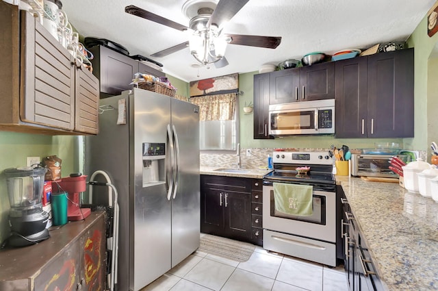 kitchen with light stone countertops, dark brown cabinetry, stainless steel appliances, sink, and light tile patterned floors