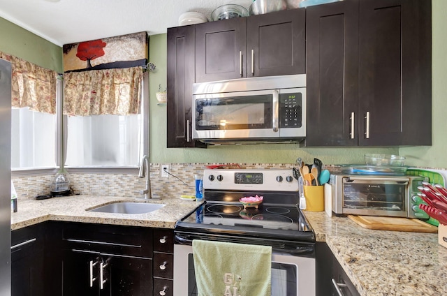 kitchen featuring sink, light stone countertops, appliances with stainless steel finishes, tasteful backsplash, and dark brown cabinets