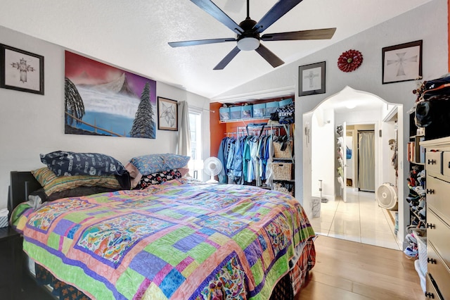 bedroom featuring ceiling fan, light hardwood / wood-style floors, a textured ceiling, lofted ceiling, and a closet