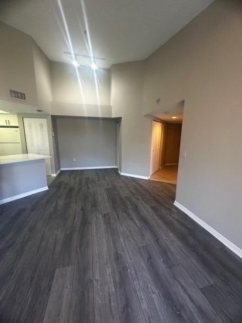 unfurnished living room with dark hardwood / wood-style flooring, a towering ceiling, and a textured ceiling