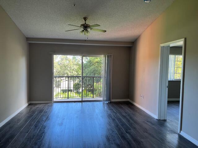 empty room with a wealth of natural light, ceiling fan, dark hardwood / wood-style flooring, and a textured ceiling