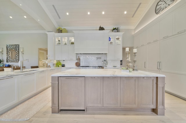 kitchen with custom exhaust hood, lofted ceiling, sink, light stone countertops, and white cabinetry