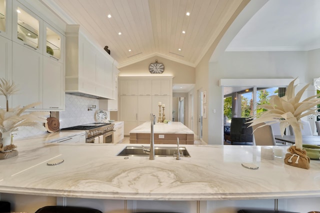 kitchen with sink, stainless steel stove, tasteful backsplash, white cabinets, and wood ceiling