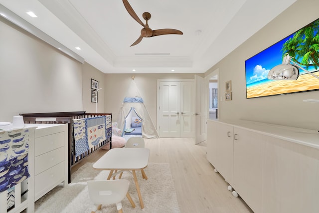 bedroom with ceiling fan, light hardwood / wood-style flooring, crown molding, a tray ceiling, and a closet