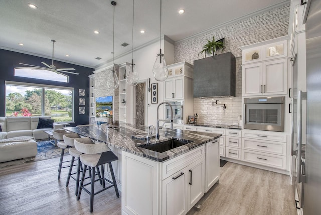 kitchen featuring sink, an island with sink, pendant lighting, stainless steel appliances, and white cabinets