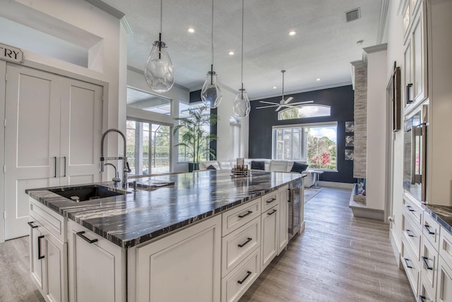 kitchen featuring pendant lighting, ornamental molding, dark stone counters, and a center island with sink