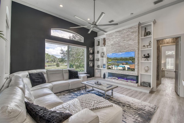 living room featuring a high ceiling, ornamental molding, ceiling fan, light hardwood / wood-style floors, and built in shelves